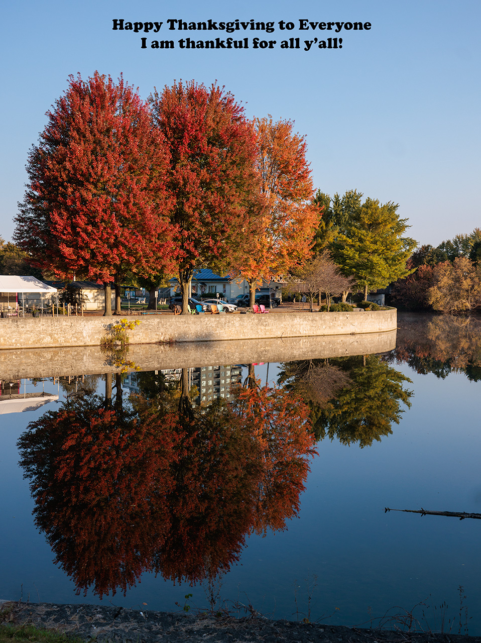 Scenic waterfront lined with vibrant autumn trees in red and gold reflecting on calm water, with houses and a walkway creating a peaceful setting among popular travel destinations.